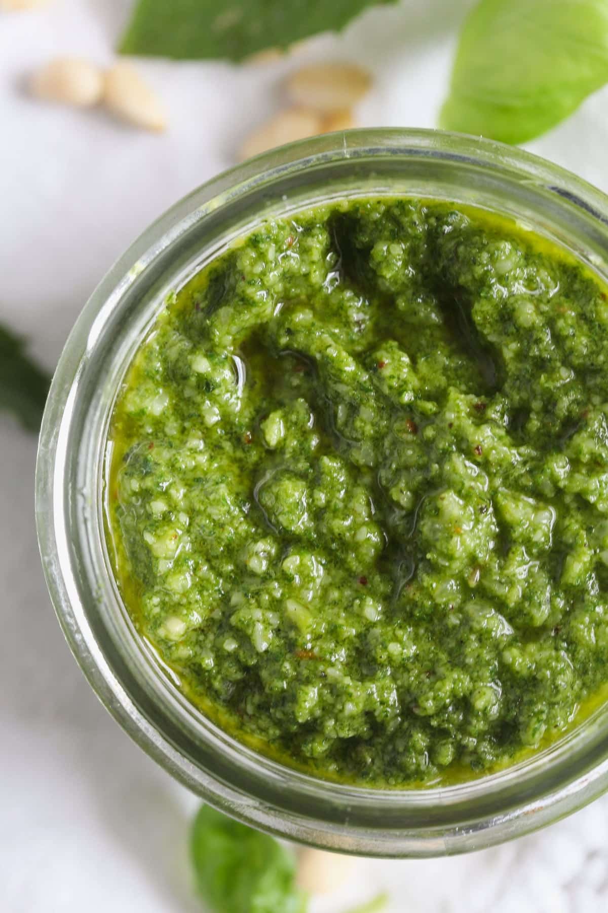 close up vibrant green pesto in a jar seen from above.