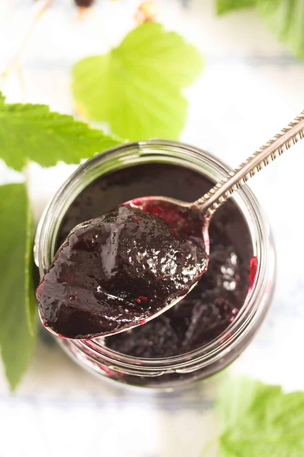 overhead view of a vintage spoon lifting blackcurrant jelly out of a jar.
