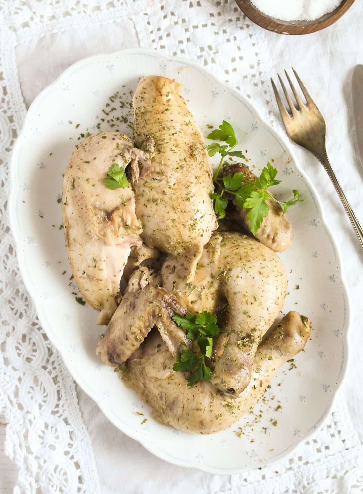 carved boiled chicken on a platter with a fork near it.