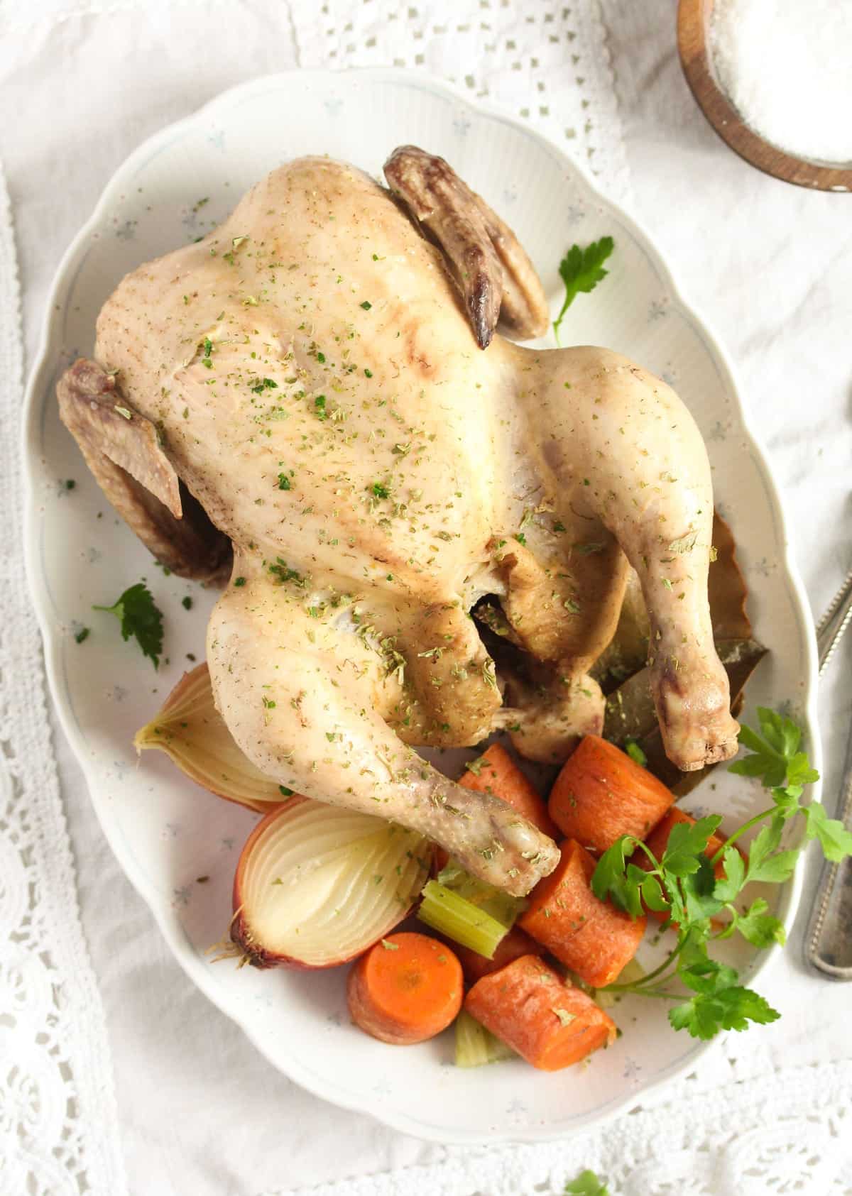 a whole boiled chicken on a platter with vegetables.