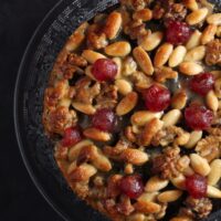 close up mincemeat cake topped with golden almonds, walnuts and cherries.