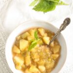 bowl of stewed rhubarb with a spoon in it and herbs on the side.