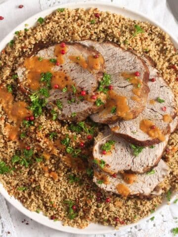 overhead view of a plate with sliced veal roast served on couscous.