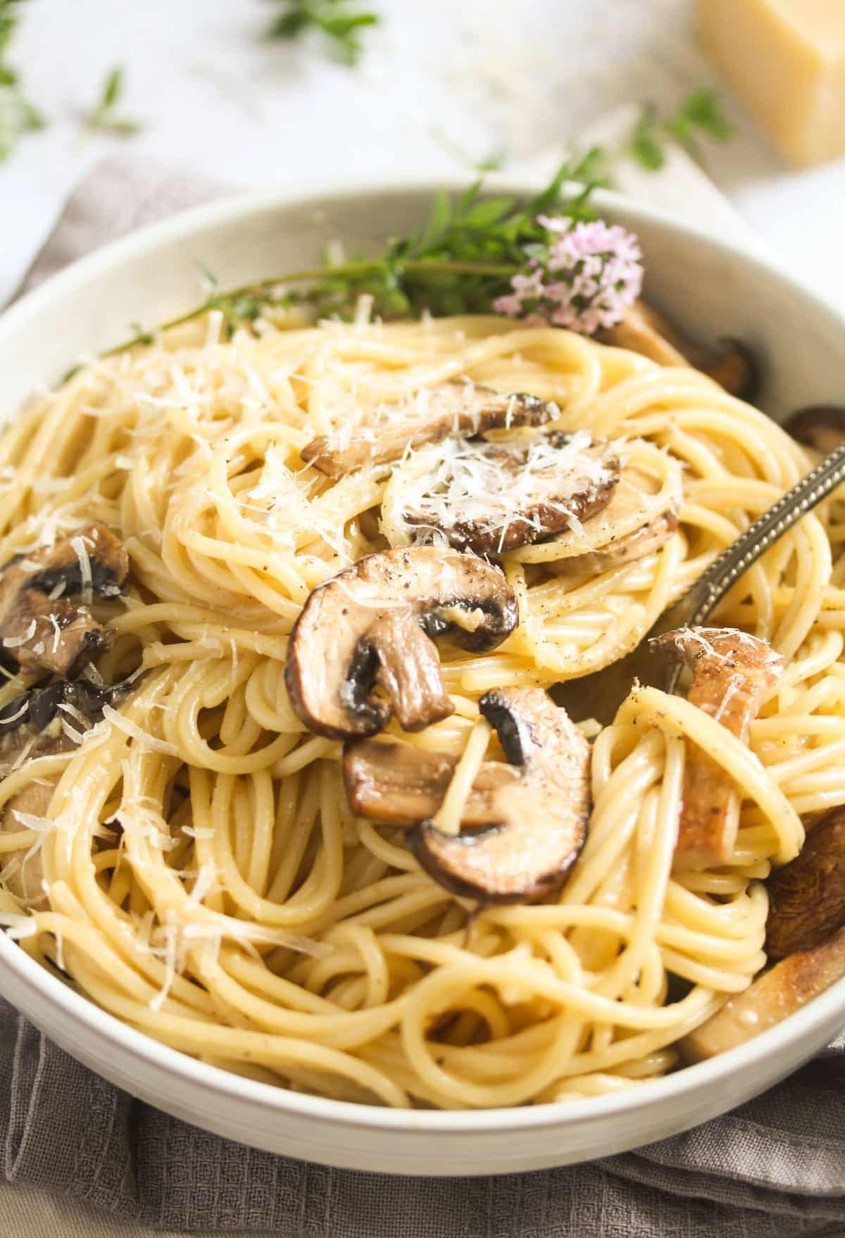close up truffled pasta with mushrooms in a white bowl.