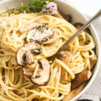 close up of a bowl full of spaghetti, mushrooms, garnished with thyme.