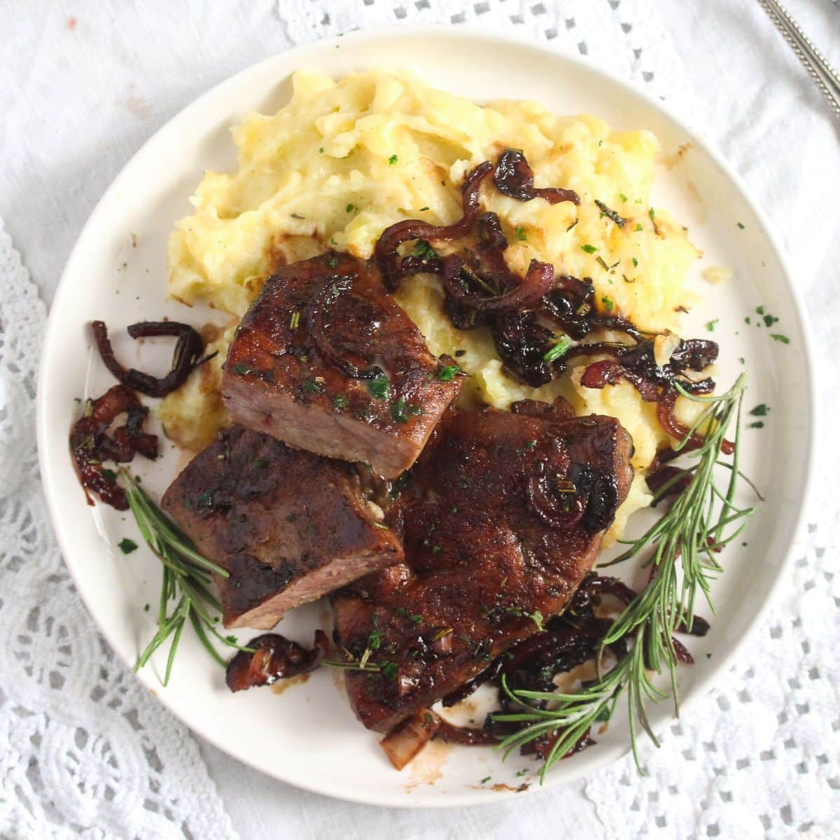 veal liver, caramelized red onions, mash and rosemary on a plate.