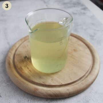 strained asparagus stock in a jug pan on a wooden board.