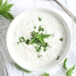 overhead view of a bowl of yogurt mint sauce on a white table cloth.