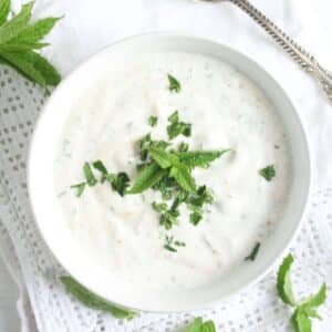 overhead view of a bowl of yogurt mint sauce on a white table cloth.