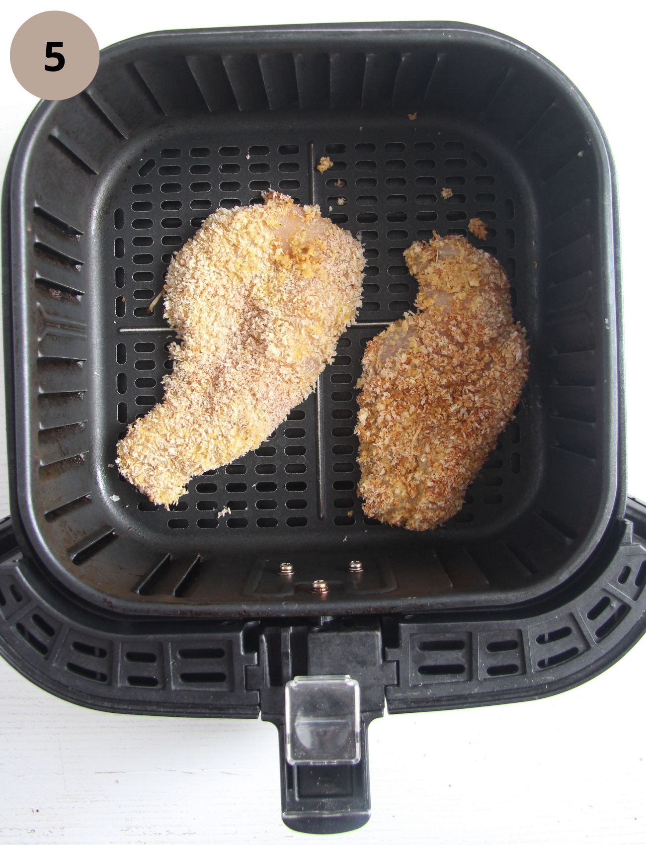 two uncooked breaded chicken slices in the basket of the air fryer.