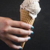 cone of ice cream held by a girl's hand with green painted nails.