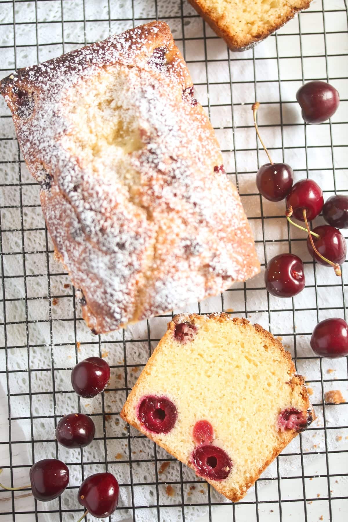 overhead view of a loaf cake on a rack sourrounded by fresh cherries.
