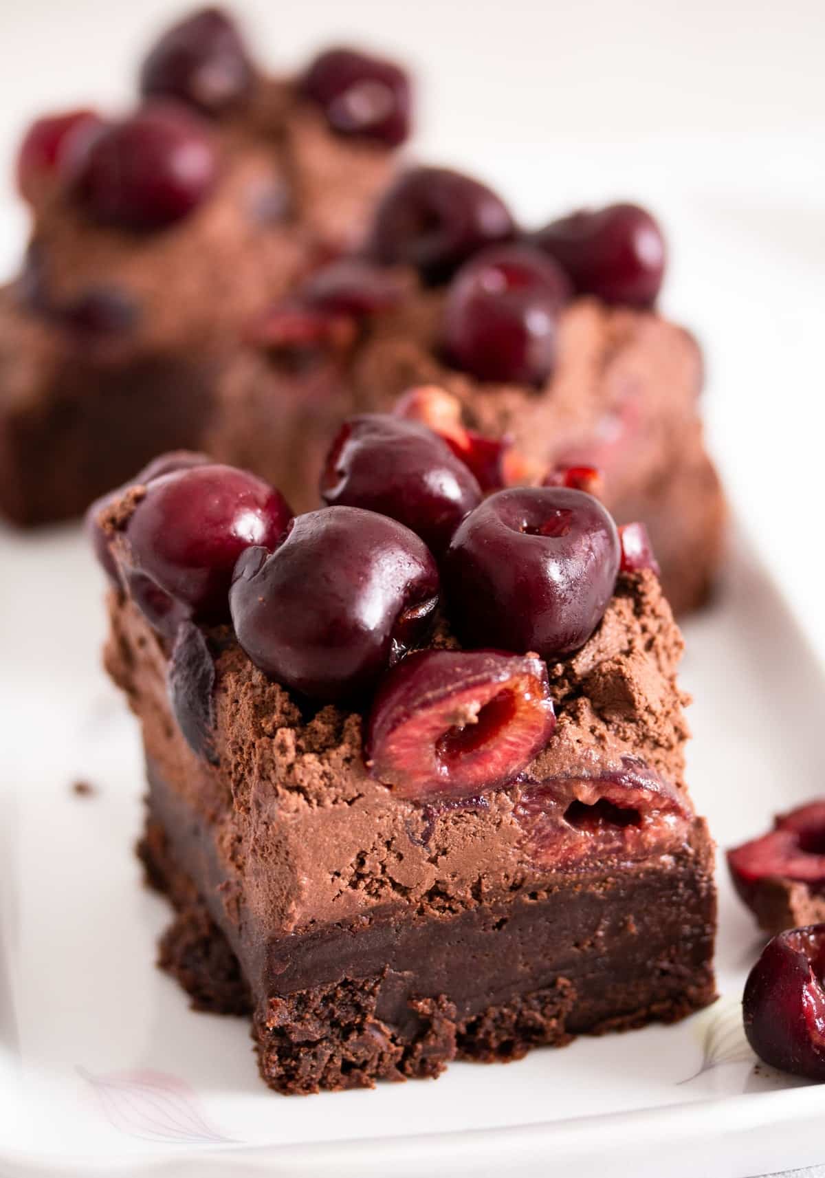 three brownies topped with ganache and fresh cherries on a platter.