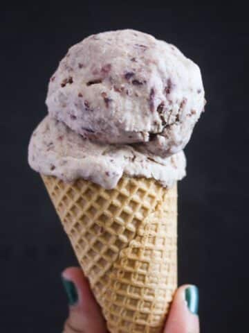 vanilla cherry ice cream in a cone on a black background.