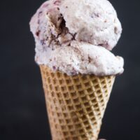 girl's hand holding cherry vanilla ice cream in a cone.