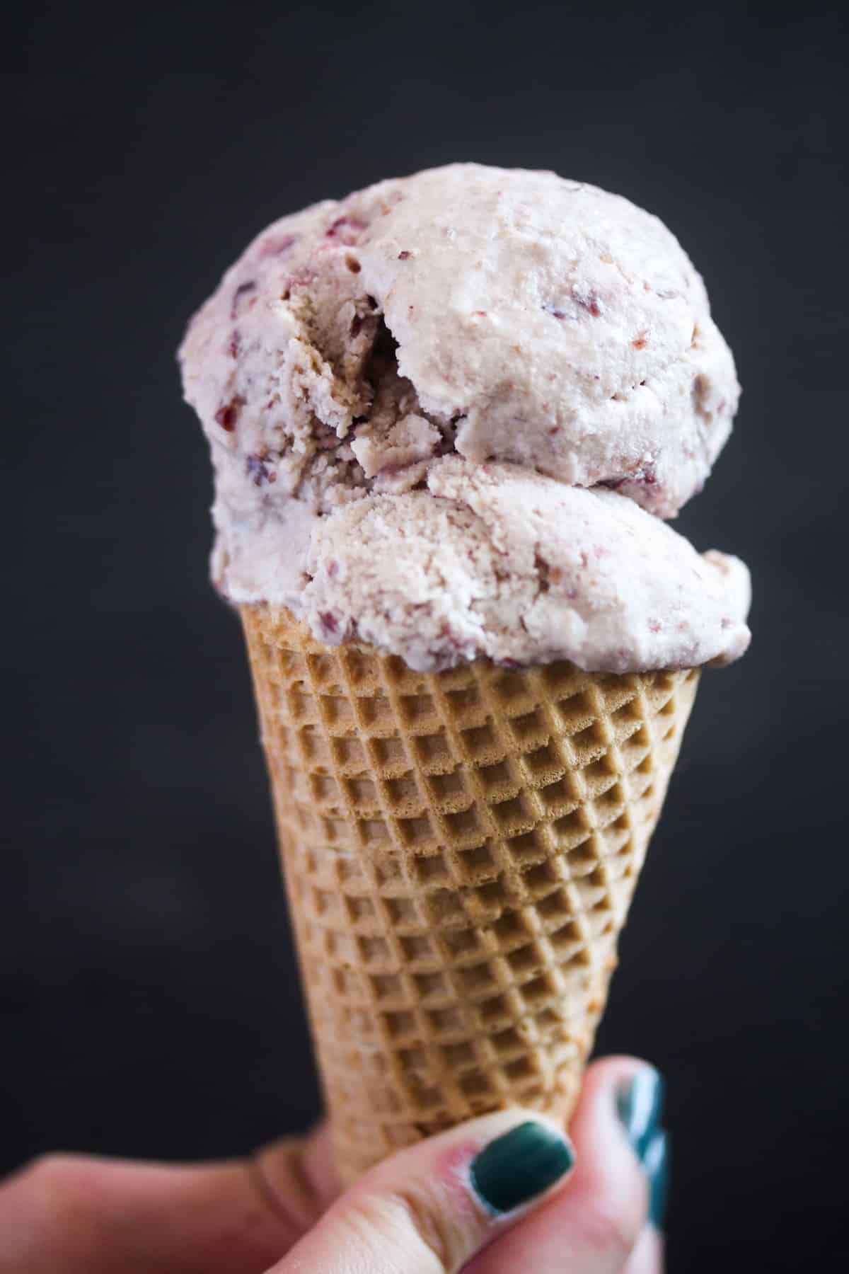 girl's hand holding cherry vanilla ice cream in a cone.