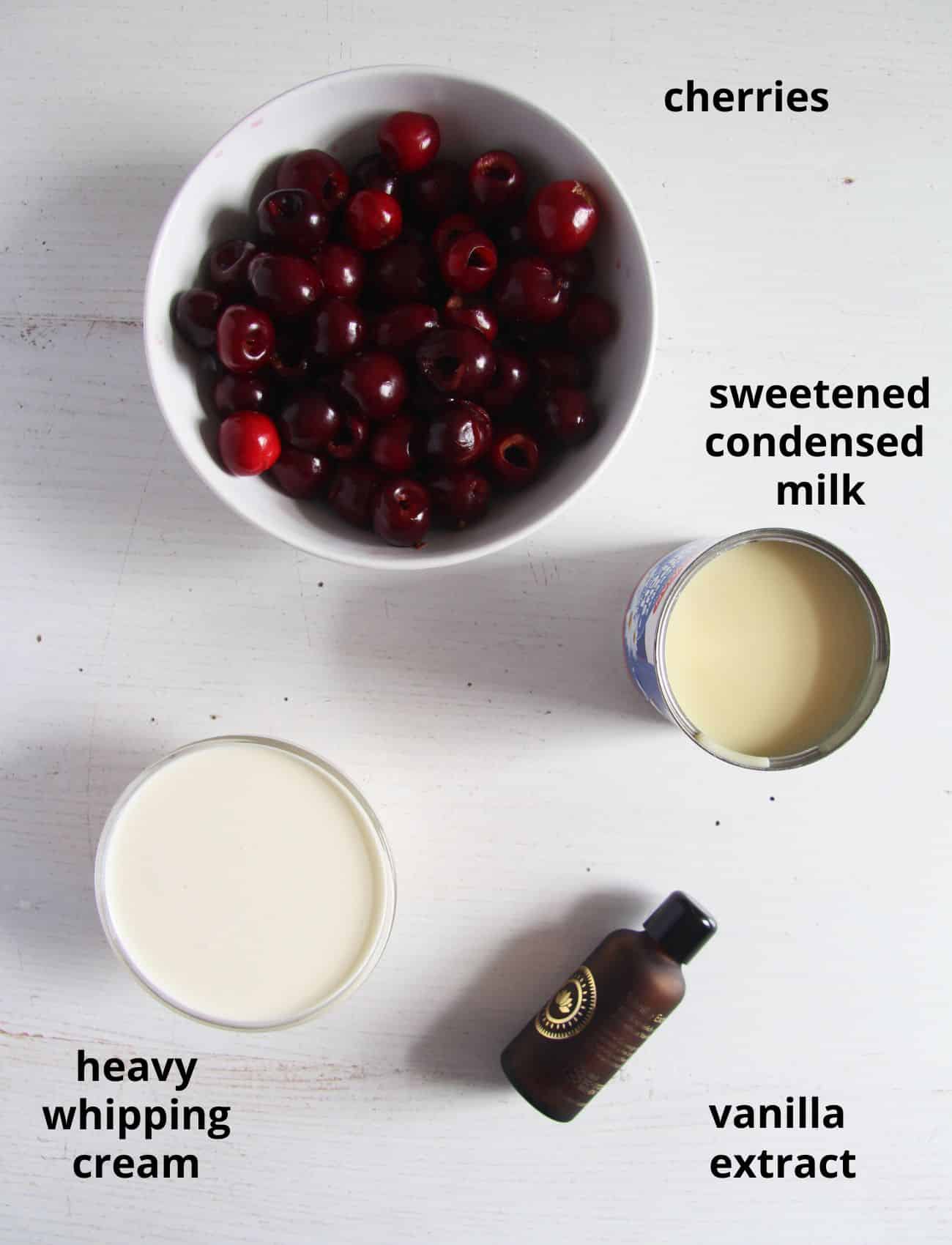 cherries, condensed milk, heavy cream and vanilla extract on a table.