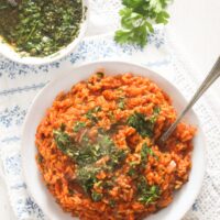 overhead view of a plate with red colored rice and a bowl of chimichurri sauce.