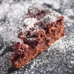 cherry chocolate cake sliced on a black board sprinkled with icing sugar.