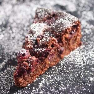 cherry chocolate cake sliced on a black board sprinkled with icing sugar.