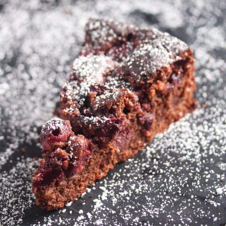 cherry chocolate cake sliced on a black board sprinkled with icing sugar.