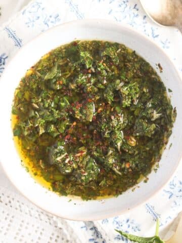 overhead view of a bowl with mint chimichurri on a white cloth with blue flowers.