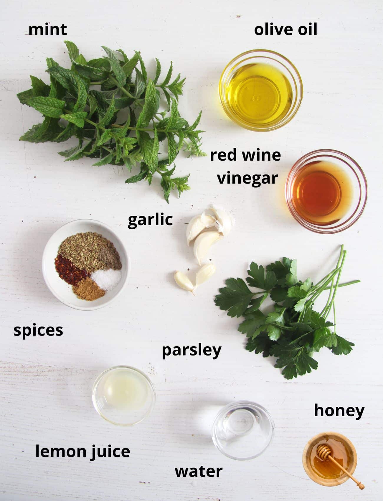listed ingredients for making chimichurri with parsley and mint on the table.