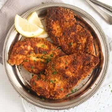 fried panko chicken breast with lemon slices on a silver plate.