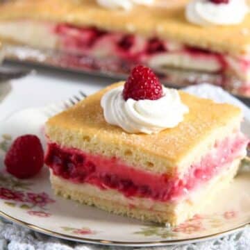 square of tangy raspberry lemon cake topped with whipped cream and a raspberry.