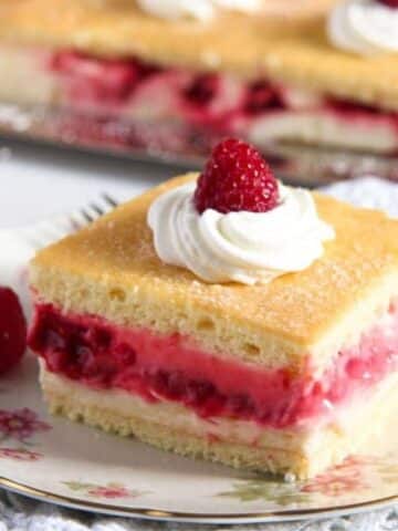 square of tangy raspberry lemon cake topped with whipped cream and a raspberry.