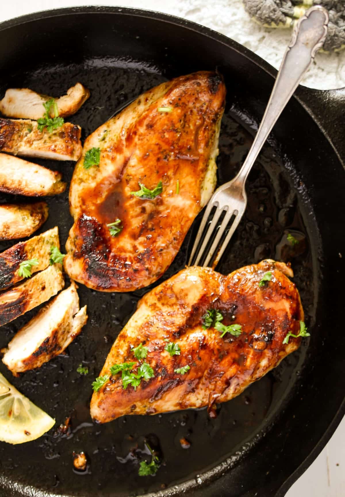 two pieces of golden chicken breast and another one sliced in a cast iron skillet.