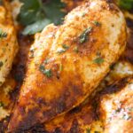 close up one piece of golden baked chicken breast and parsley leaves.