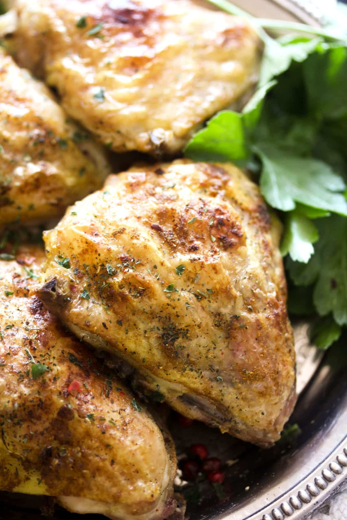 close up golden cooked chicken thighs with parsley leaves.