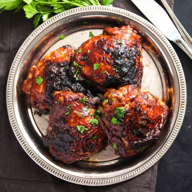 oven baked bbq chicken thighs on a small silver plate.