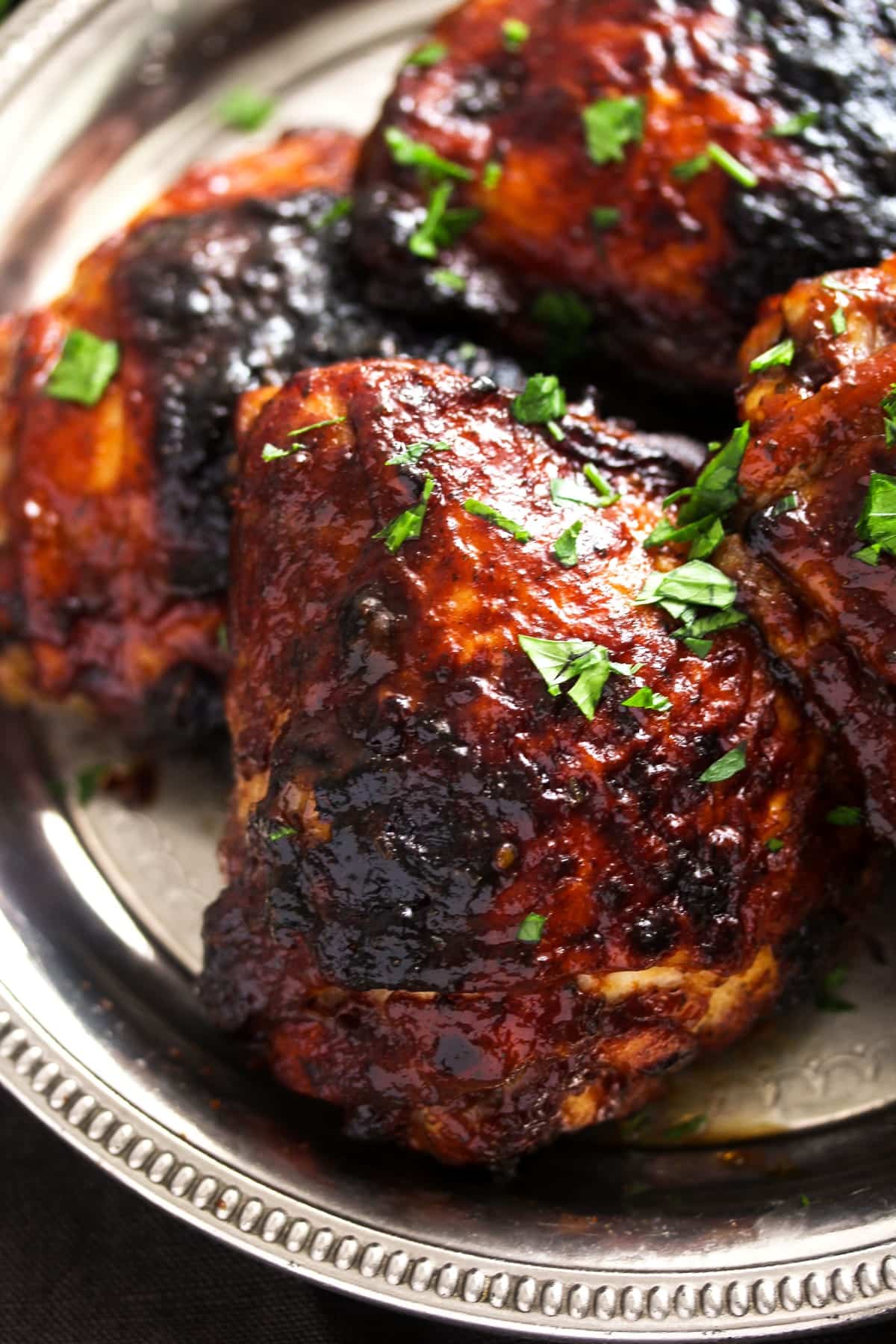 close up one sticky glazed chicken thigh sprinkled with parsley.