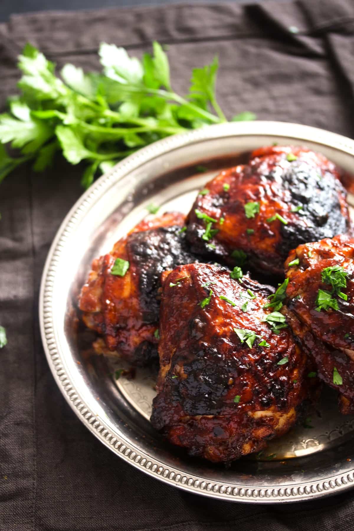 baked chicken thighs with bbq sauce on a dark background with parsley.