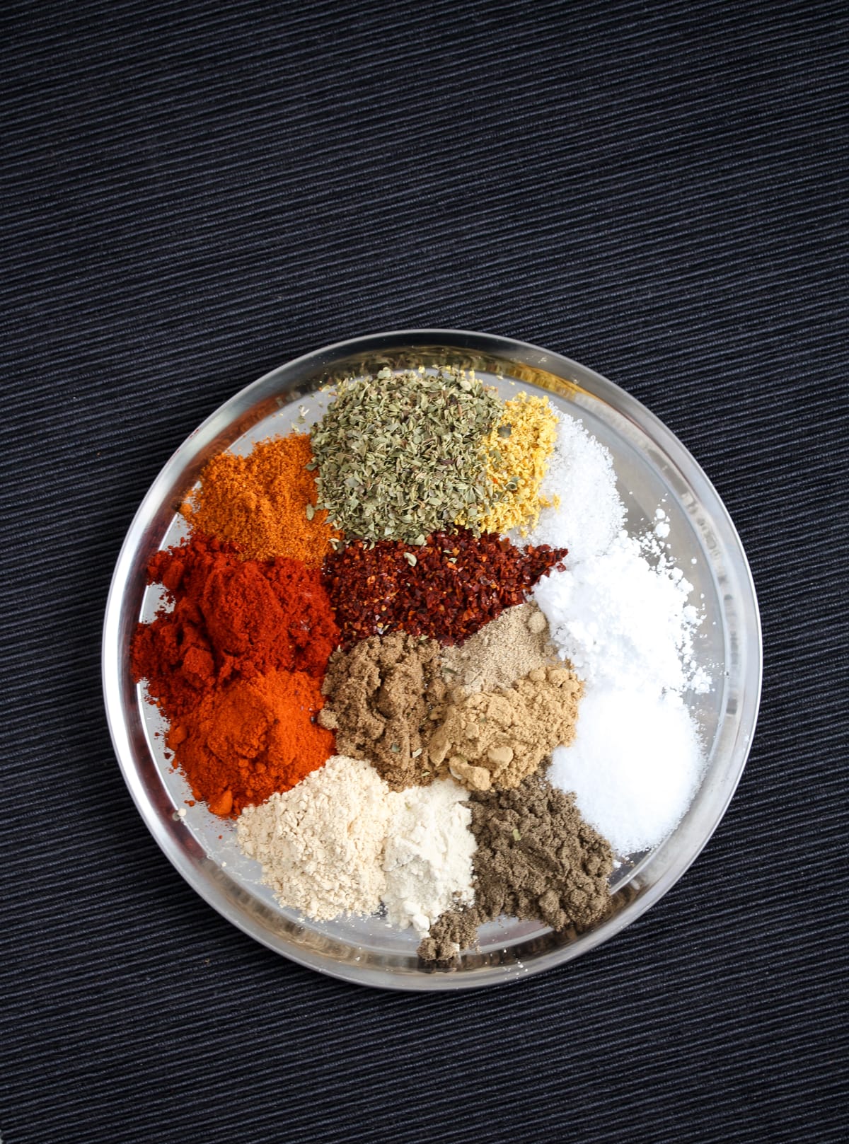 many different spices for peri peri seasoning on a small silver plate.