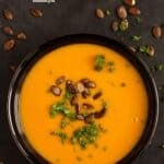 pinterest image of pumpkin soup with pepitas and ginger on a black background.