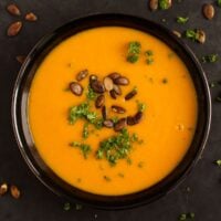 overhead view of a bowl with pumpkin ginger soup sprinkled with roasted pepitas and parsley.