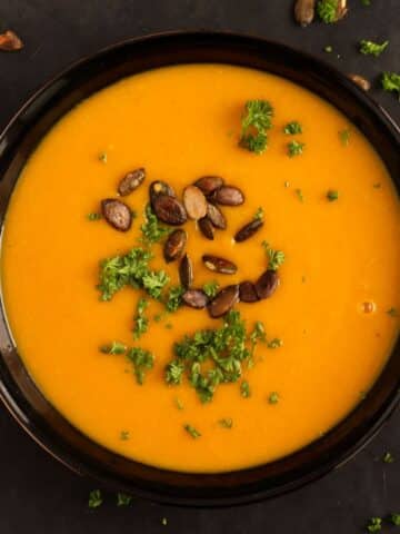 overhead view of a bowl with pumpkin ginger soup sprinkled with roasted pepitas and parsley.