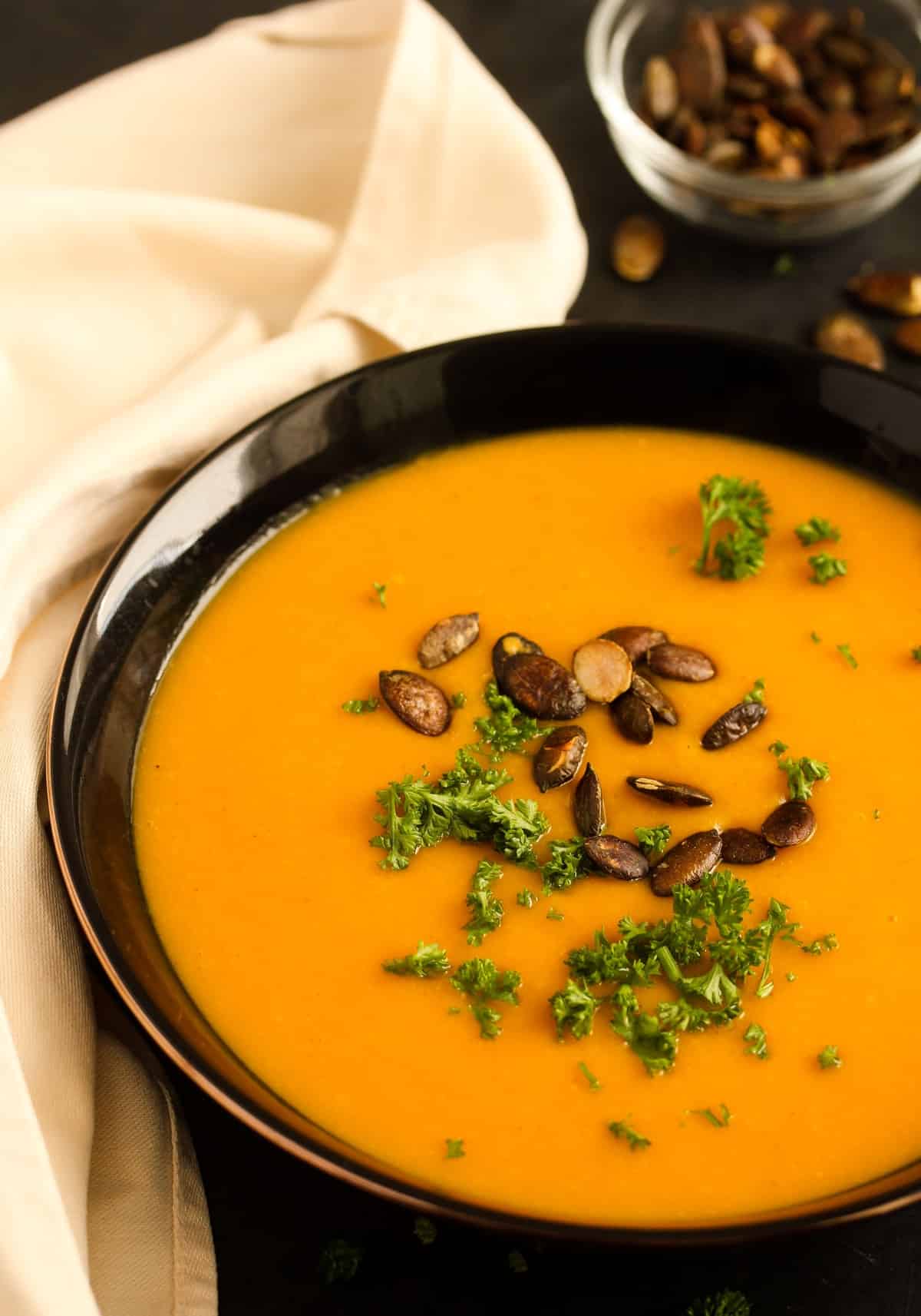 close up of a brown bowl full of soup with butternut squash, ginger and pumpkin seeds.