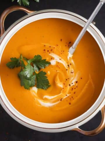 overhead view of a bowl of slow cooker pumpkin soup with parsley and cream.