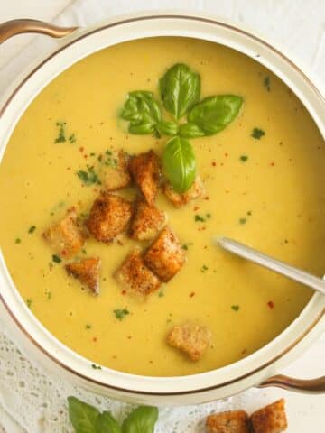 vintage bowl full with green tomato soup topped with croutons and basil.