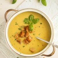 bowl of green tomato cream soup topped with croutons and basil.