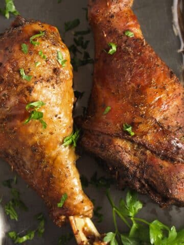 close up slow cooker turkey legs sprinkled with parsley.