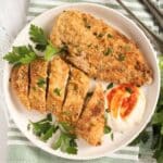 overhead view of a plate with two breaded baked chicken cutlets one sliced.
