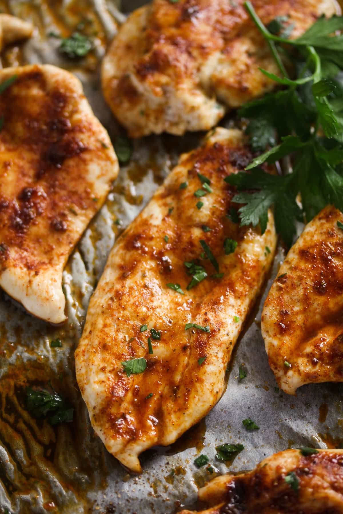 slices of chicken breast on a baking sheet with parsley.