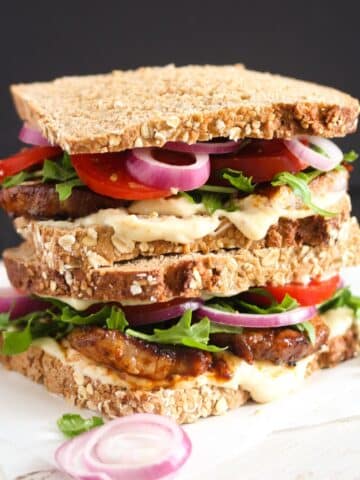 pork belly sandwich with mayonnaise, rocket, tomatoes and onions.