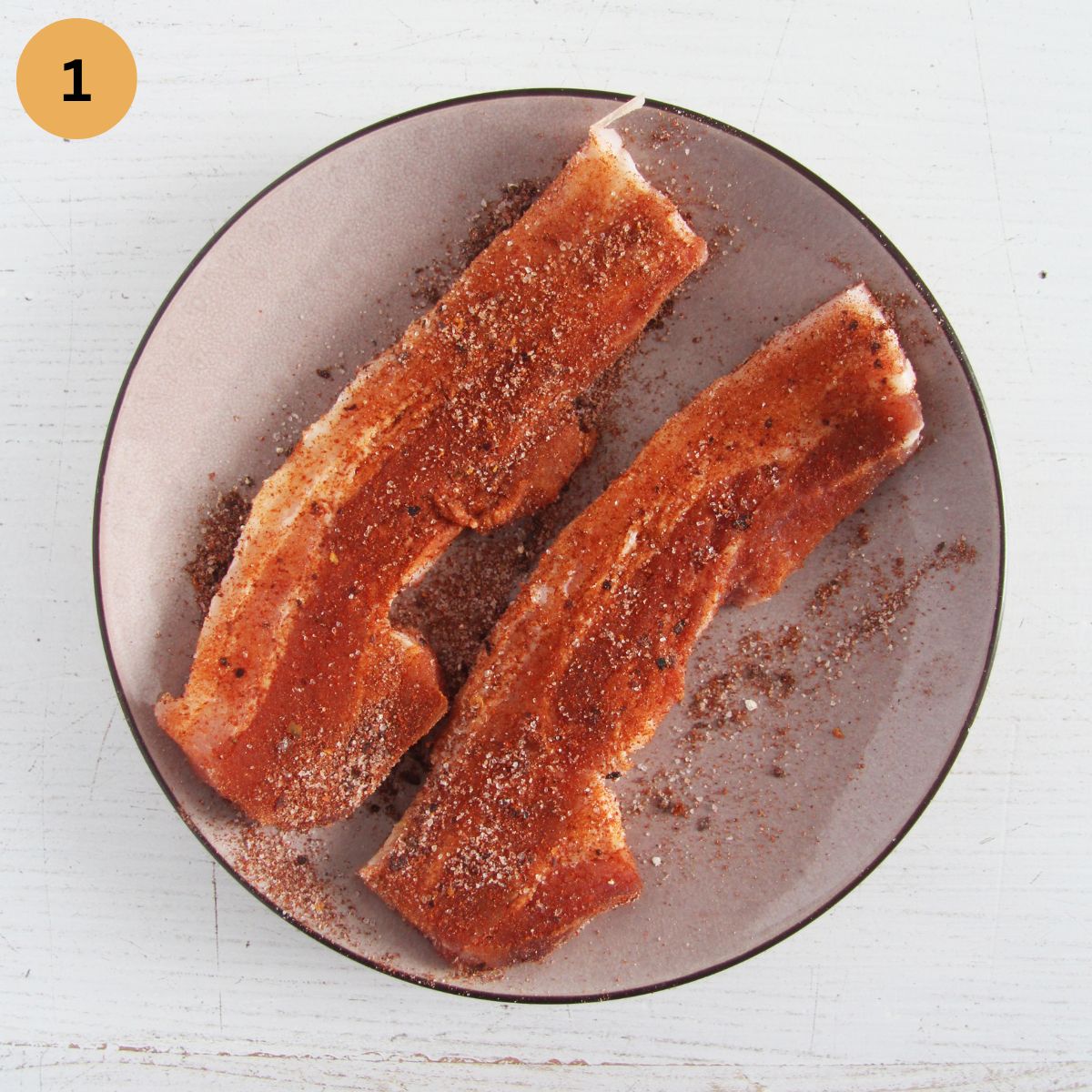 two slices of seasoned pork belly on a small plate.