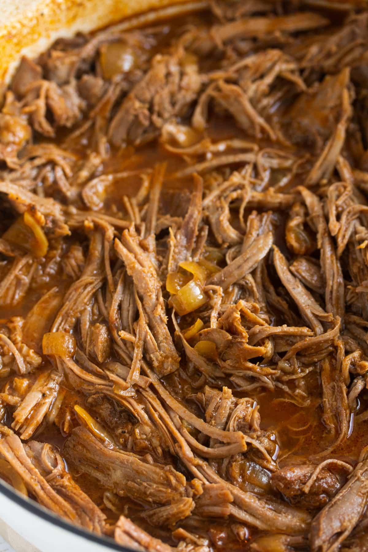 close up of shredded turkey meat in a pot with onions and gravy.
